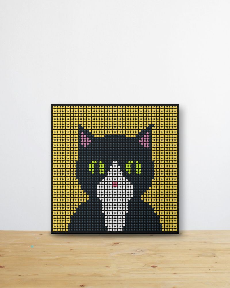 A tuxedo cat mosaic on a yellow background leaning on a wooden desk